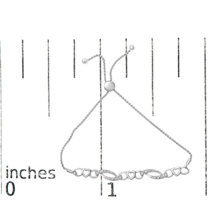 White metal bracelet with intertwined heart shapes and curved links set with small white gemstones, displayed flat on a ruler for size reference, top-down angle.