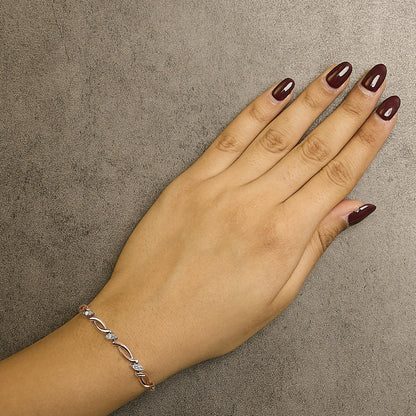 Close-up overhead shot of a wrist wearing a rose-colored bracelet featuring alternating marquise-shaped links and round white gemstones in pave setting.