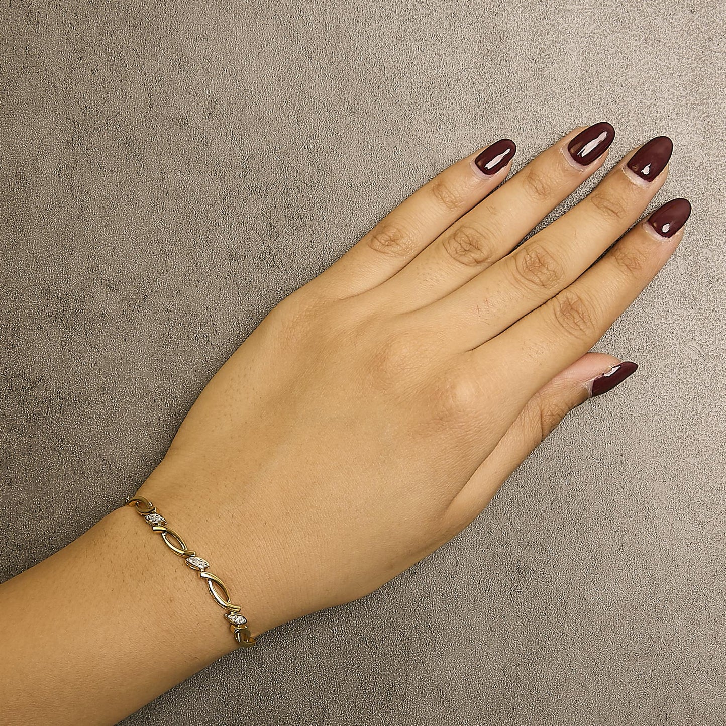 Close-up angled top view of a yellow metal bracelet with small white round pave-set gemstones worn on a model's wrist.