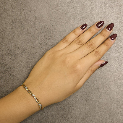 Close-up angled top view of a yellow metal bracelet with small white round pave-set gemstones worn on a model's wrist.