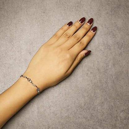 Rose-colored bracelet with white round pave gemstones forming a delicate heart and wave pattern, shown on a model's wrist from top-down angle.