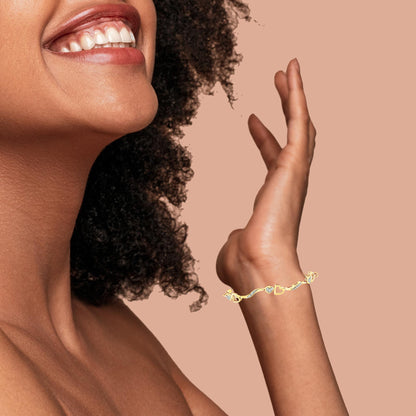 Yellow metal bracelet with heart-shaped elements and white gemstones in pave setting, shown on a model's wrist with an upward hand pose, angled side view.