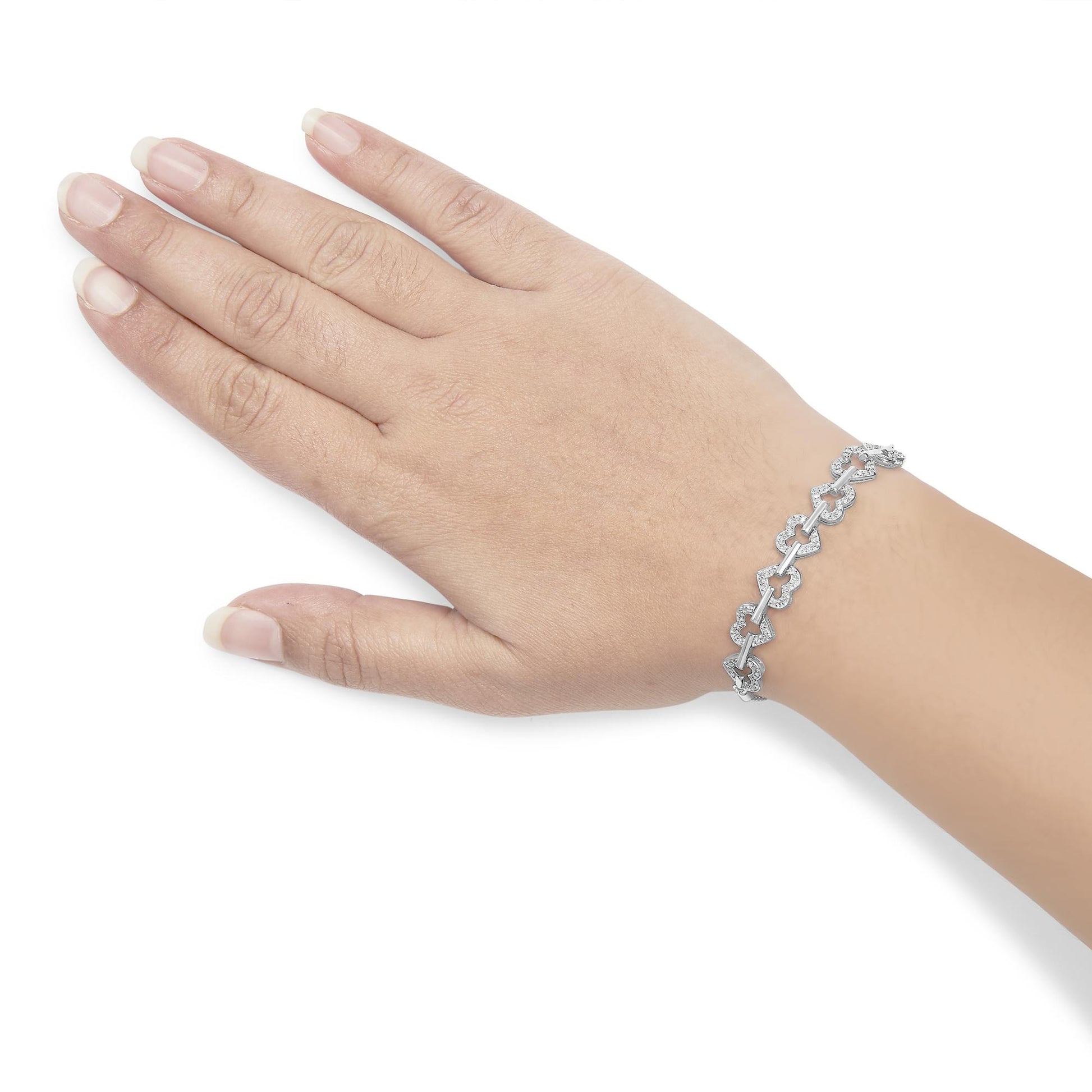White metal bracelet with linked heart shapes set with round white gemstones in prong settings, worn on a model’s left wrist, shown from an overhead angle.