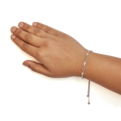 White metal bracelet with round white gemstones in prong settings, worn on a model's wrist, shown from a top angle.