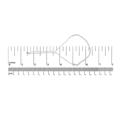 White metal bracelet with round white gemstones in prong settings, laid flat on a ruler for size reference, top-down view.