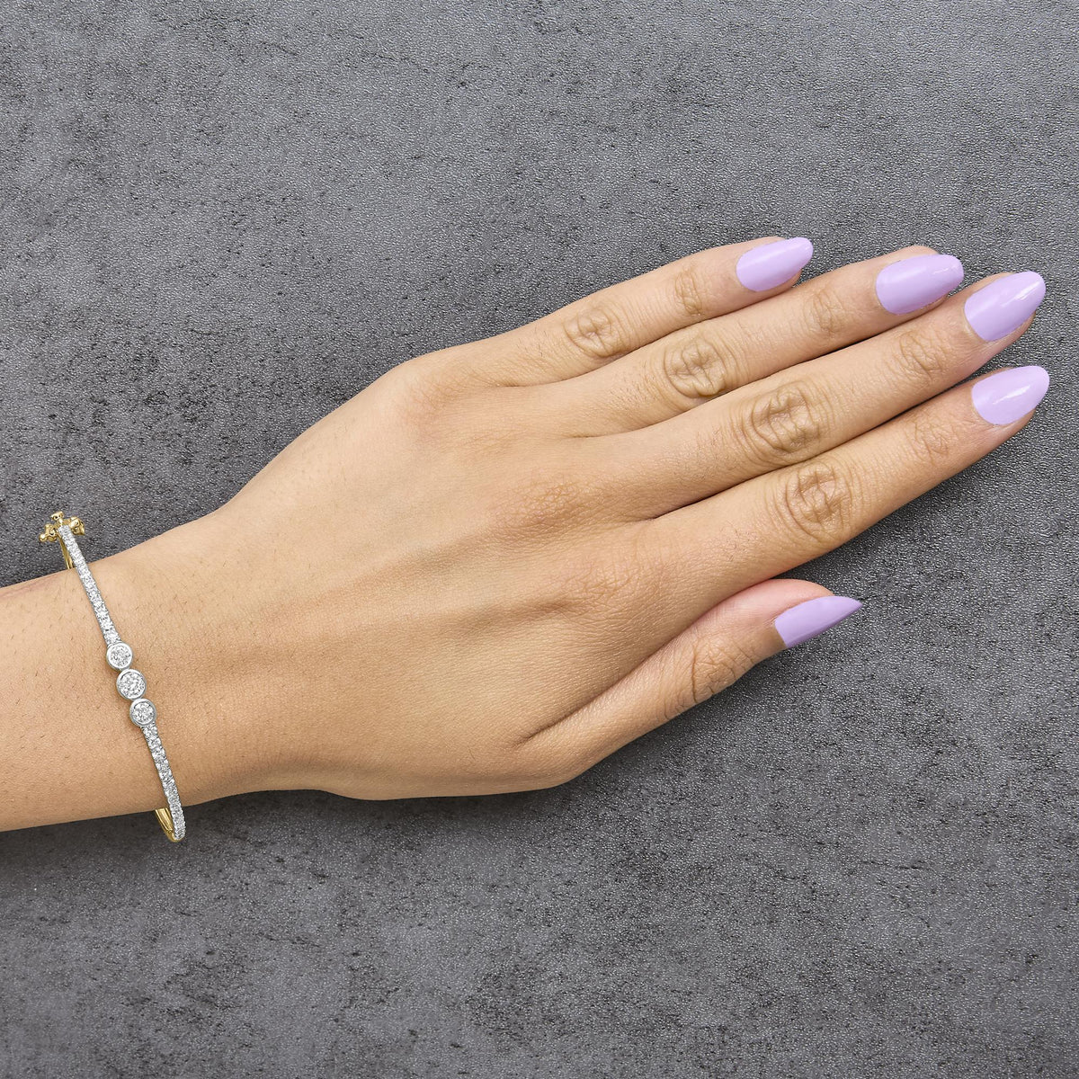Close-up front angle of a yellow metal bracelet with multiple round white gemstones in prong settings, shown worn on a model's wrist.