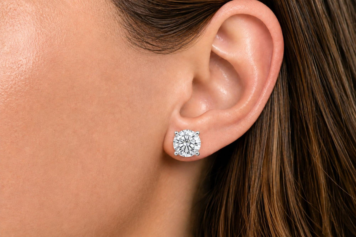 Close-up side view of a model wearing a pair of white metal stud earrings featuring round white gemstones in a four-prong setting.