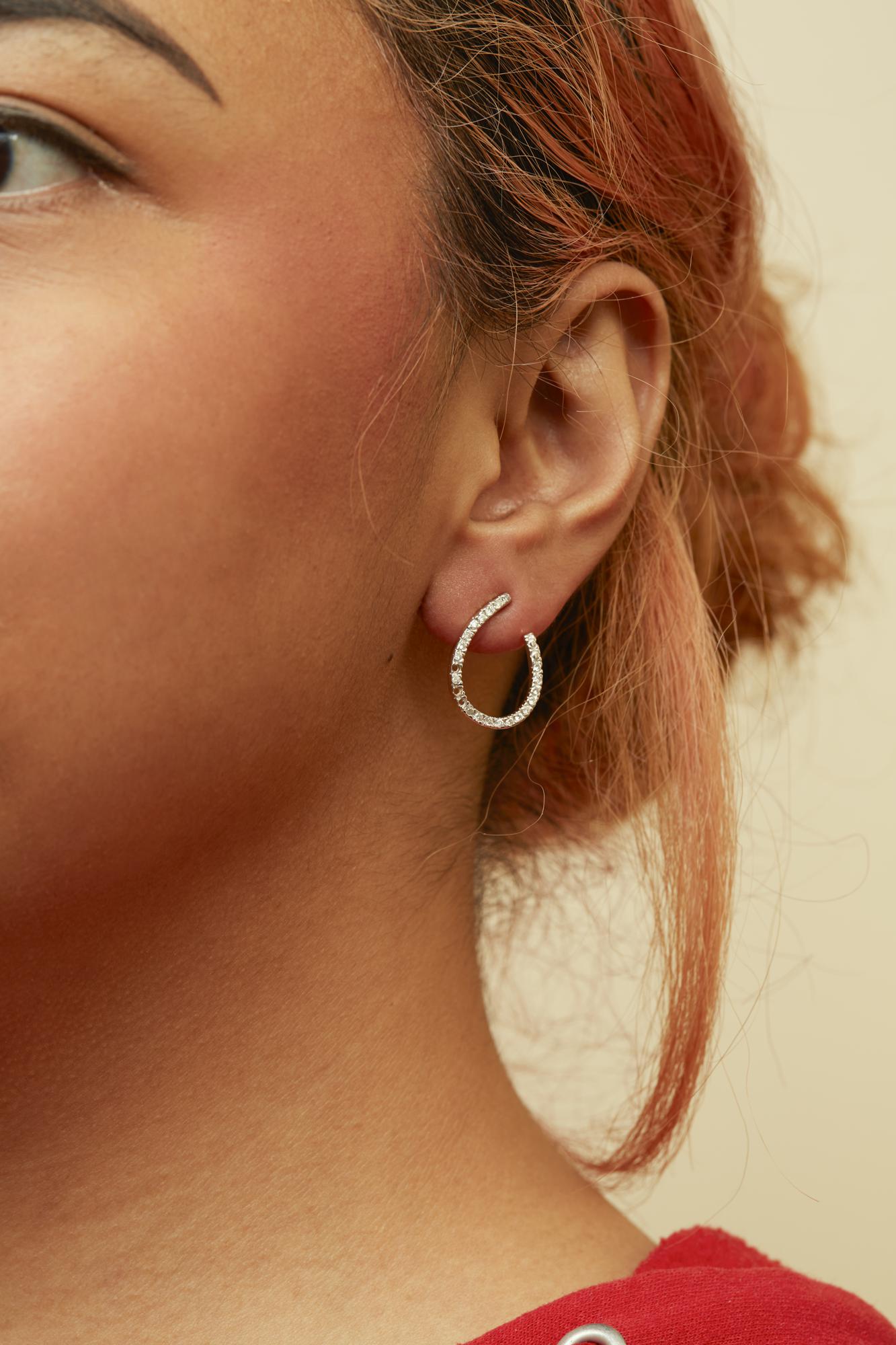 Close-up side view of a model wearing a yellow metal hoop earring adorned with prong-set white round gemstones.
