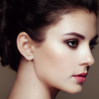Close-up side profile of a model wearing small yellow metal hoop earrings with channel-set white round gemstones.