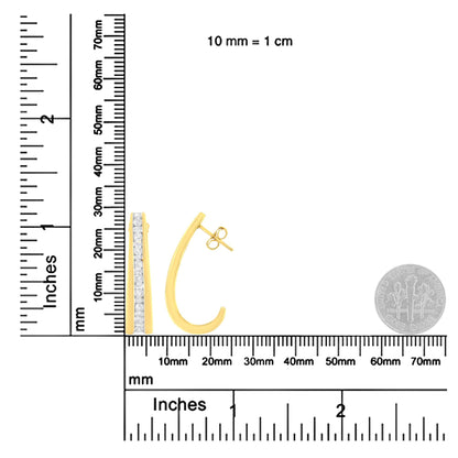 Pair of yellow metal earrings with channel-set white round and baguette gemstones, shown on a ruler and scale for size reference, front and side view.