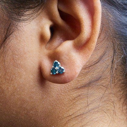 Close-up side view of a white metal earring with three round blue gemstones in a prong setting, worn on a model's ear.