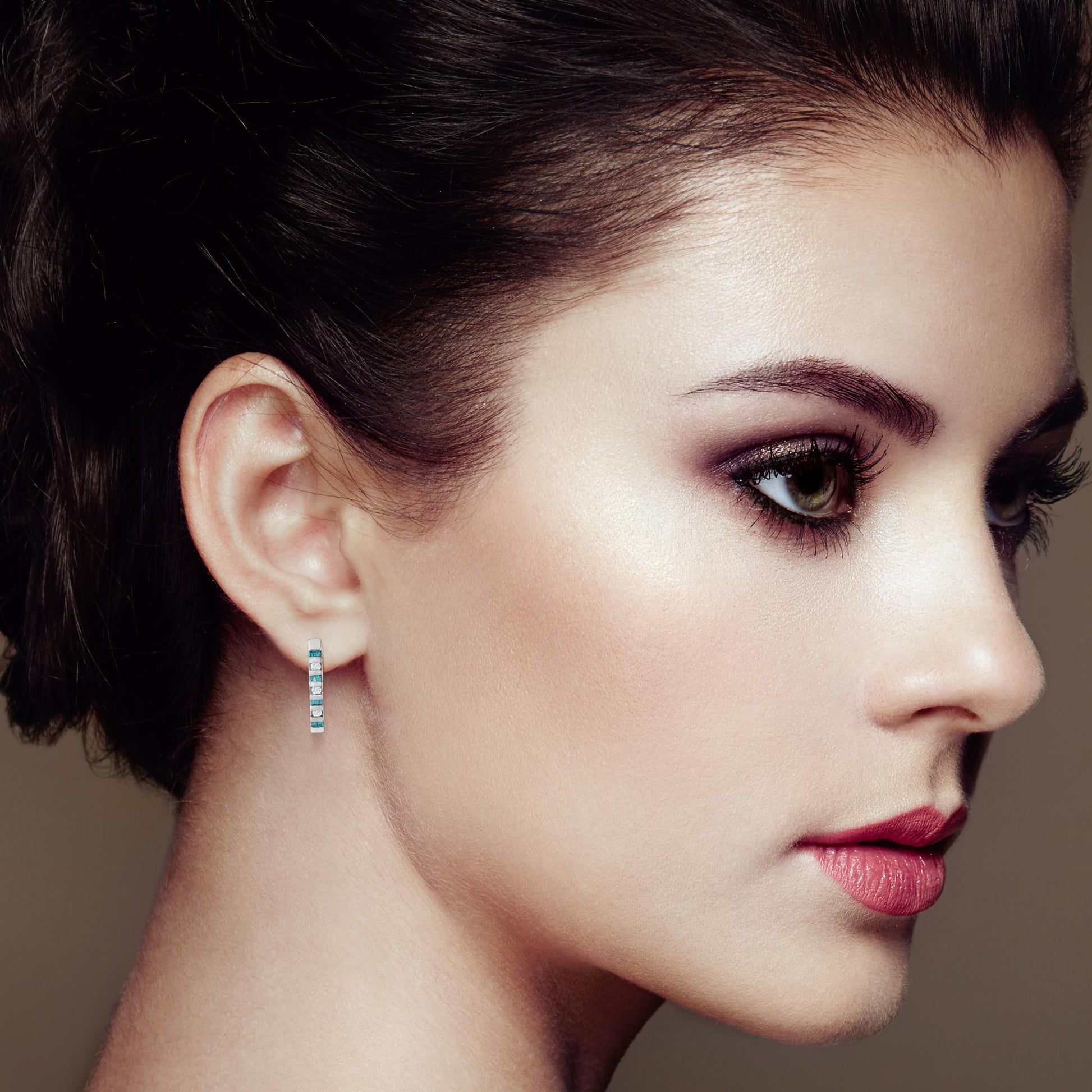 Close-up side profile of a model wearing white metal earrings with channel-set round white gemstones and baguette-shaped blue gemstones.
