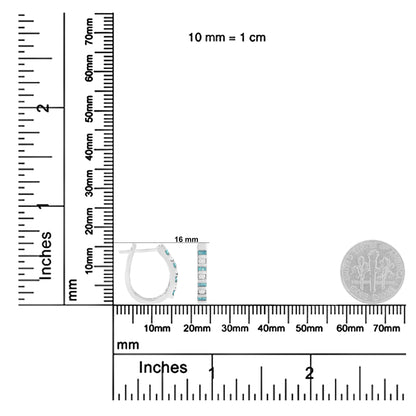 Pair of white metal earrings with round white and baguette blue gemstones in channel settings, shown from a side and front view on a ruler for size reference.