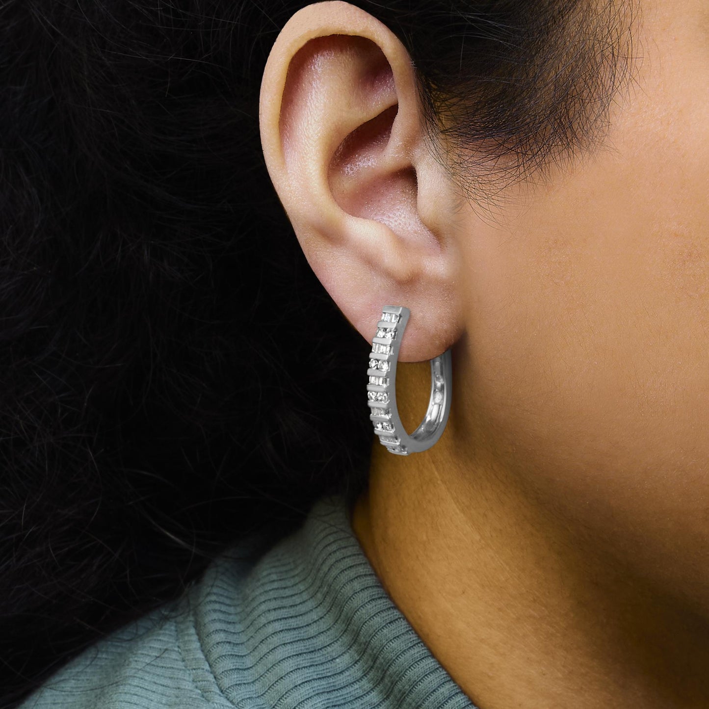 Close-up side view of a white metal hoop earring on a model's ear, featuring channel-set round and baguette white gemstones.