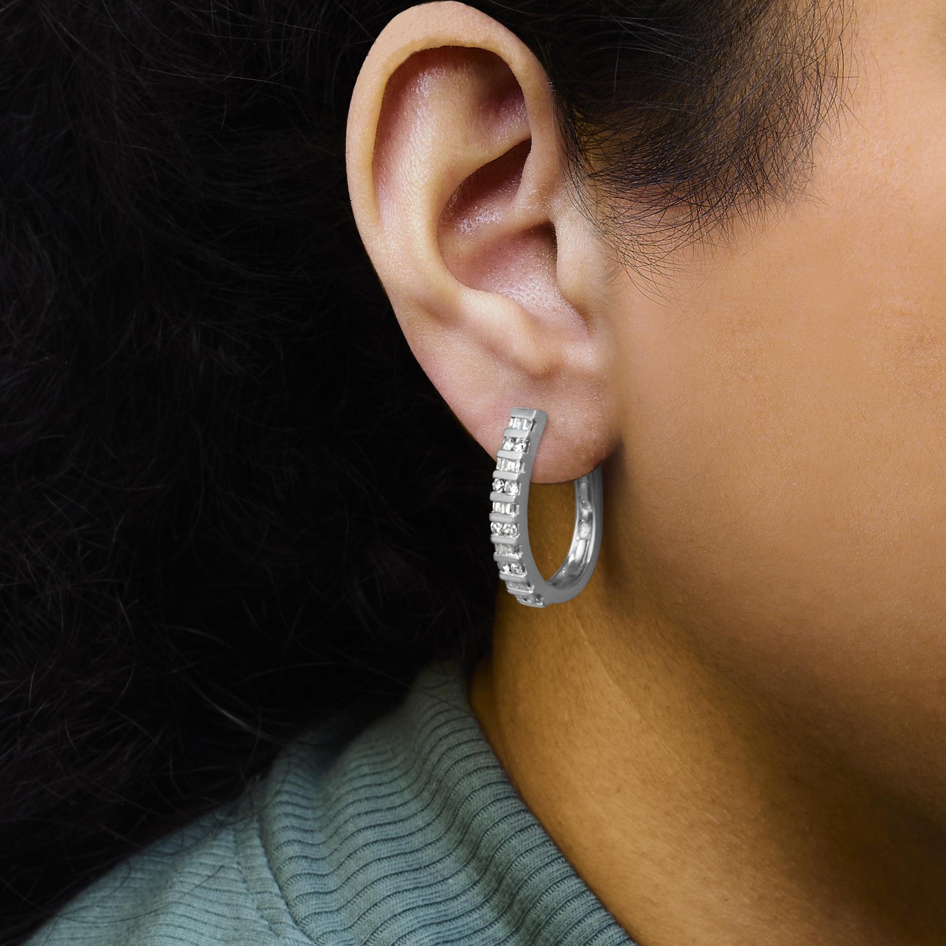 Close-up side view of a white metal hoop earring on a model's ear, featuring channel-set round and baguette white gemstones.