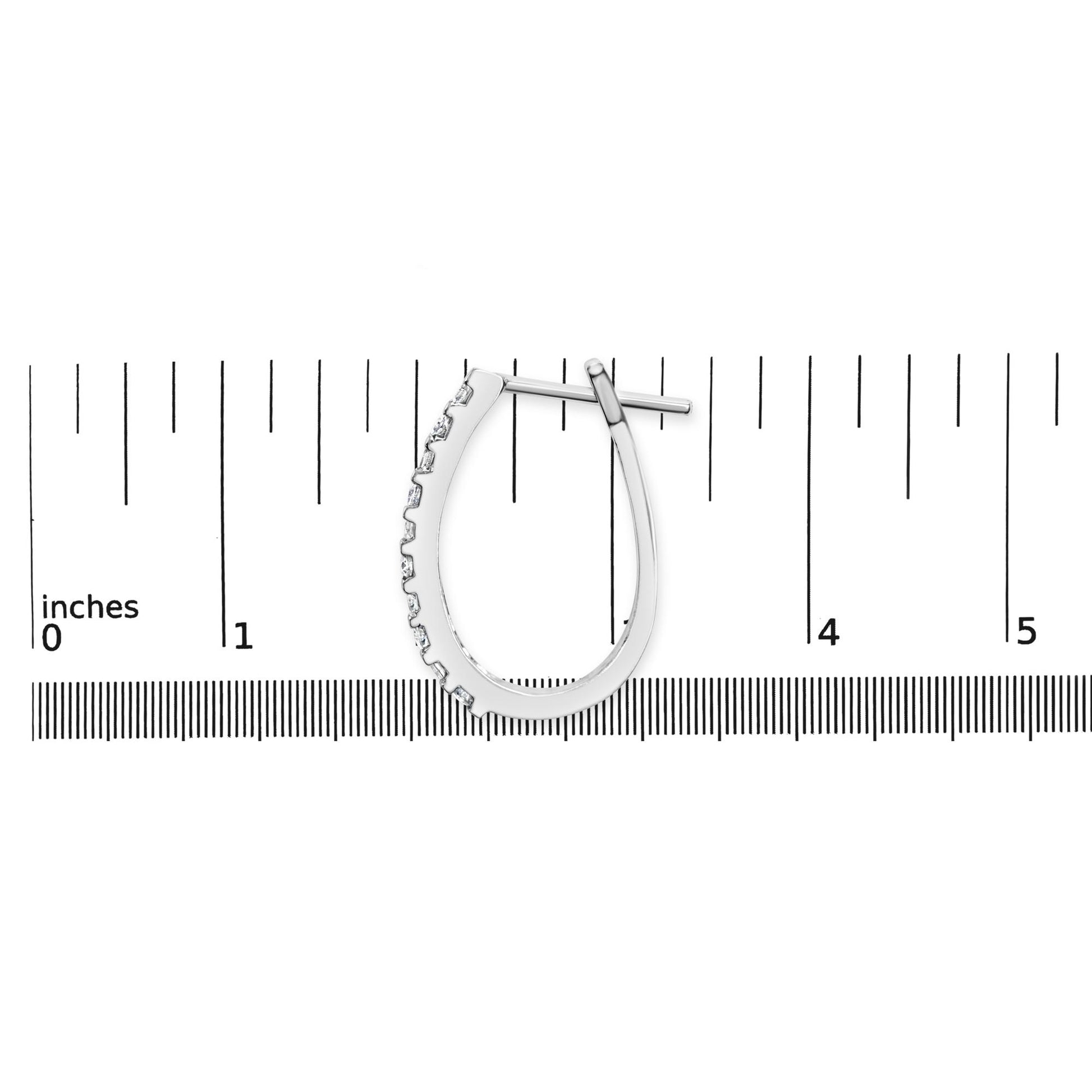 Single white metal earring with channel-set round and baguette white gemstones, displayed flat on a ruler for size reference, top-down angle.