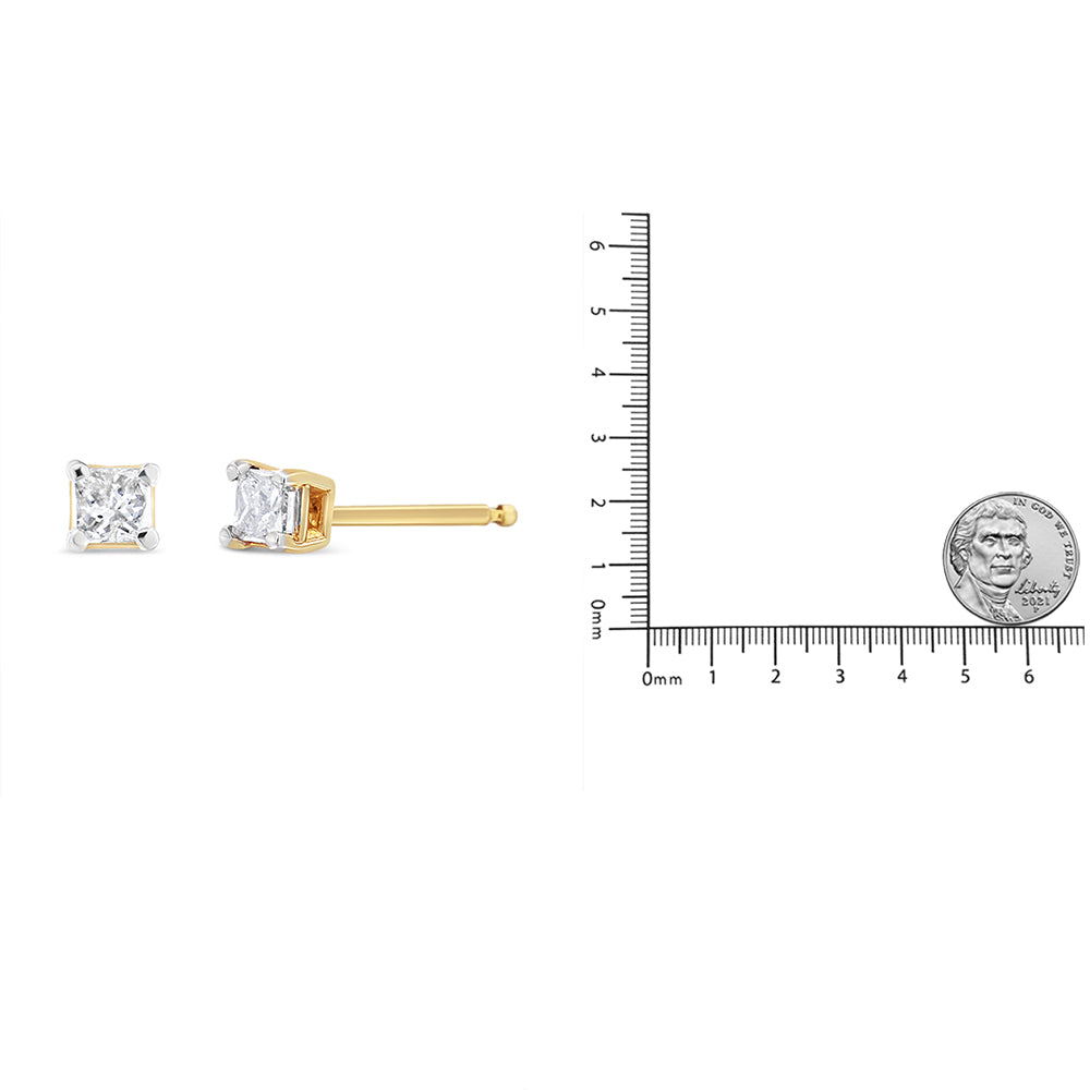 Pair of yellow metal stud earrings with princess-shaped white gemstones in 4-prong settings, one shown from the front and one from the side, displayed next to a ruler and coin for size reference.