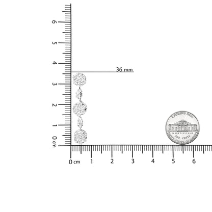 White metal drop earring with multiple round white gemstones in prong settings, shown on a ruler and next to a coin for size reference, photographed from the side.