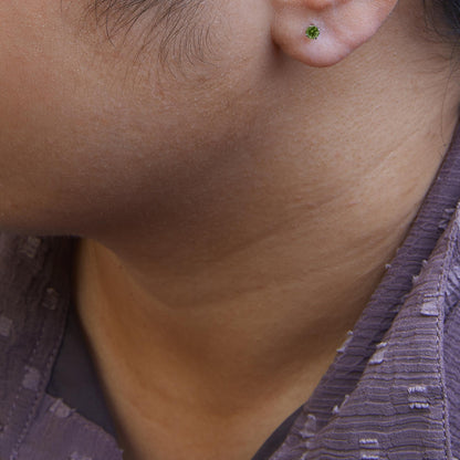 Close-up side view of a model wearing a white metal stud earring with a round green gemstone in a prong setting.