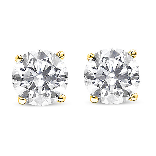 Close-up front view of a pair of yellow metal stud earrings each set with a round white gemstone in a prong setting.
