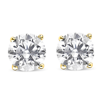 Close-up front view of a pair of yellow metal stud earrings each set with a round white gemstone in a prong setting.