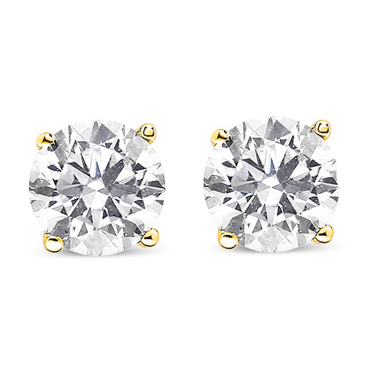Close-up front view of a pair of yellow metal stud earrings each set with a round white gemstone in a prong setting.