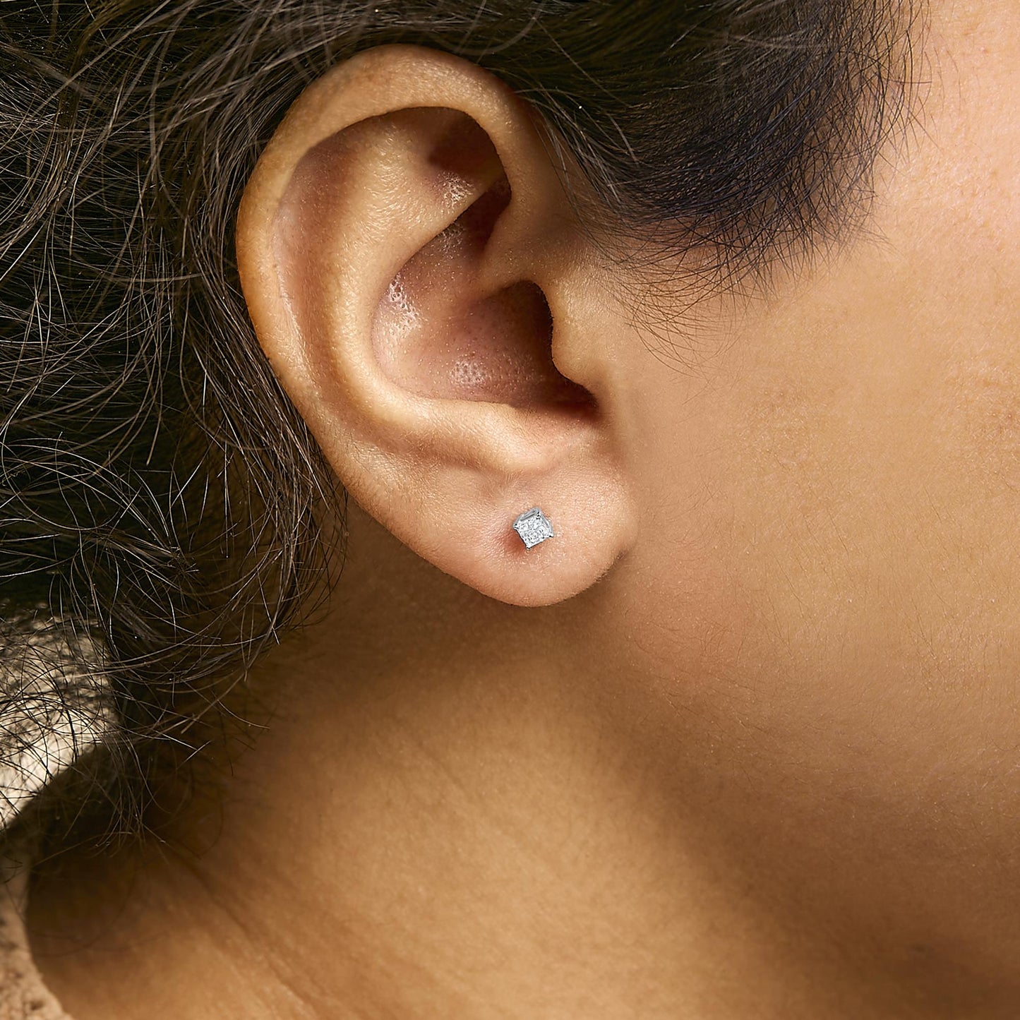 Close-up side view of a white metal earring with a princess-shaped white gemstone in prong setting worn on a model's ear.