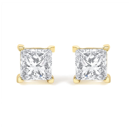 Front view of a pair of yellow metal stud earrings each featuring a princess-shaped white gemstone in a four-prong setting.
