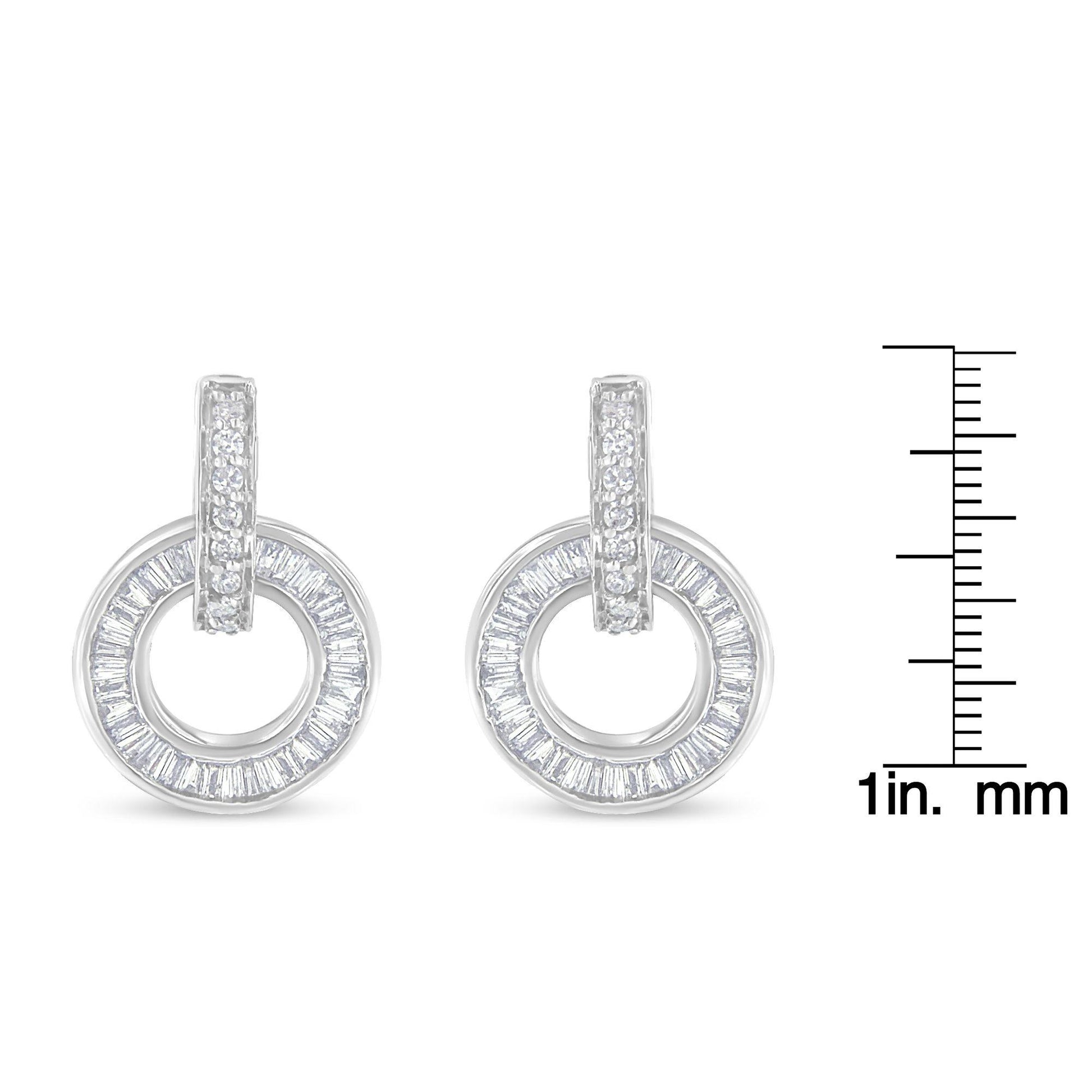 Front-facing view of white metal circular earrings with a row of round white gemstones set on the vertical bar and baguette-shaped white gemstones arranged in a circle, displayed next to a ruler for size reference.