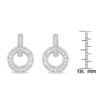 Front-facing view of white metal circular earrings with a row of round white gemstones set on the vertical bar and baguette-shaped white gemstones arranged in a circle, displayed next to a ruler for size reference.