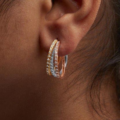Close-up side view of a person's ear wearing a tri-color hoop earring with yellow, white, and rose metal bands, each set with round white gemstones in prong settings.