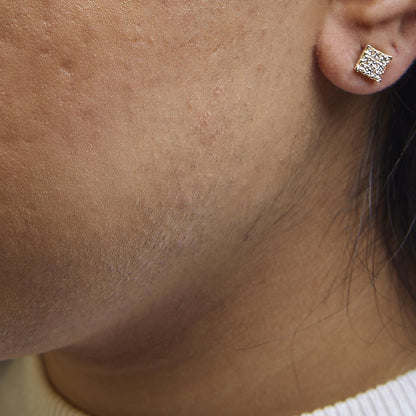 Close-up side view of a yellow metal earring with multiple white princess-shaped gemstones in an invisible setting, worn on a model.