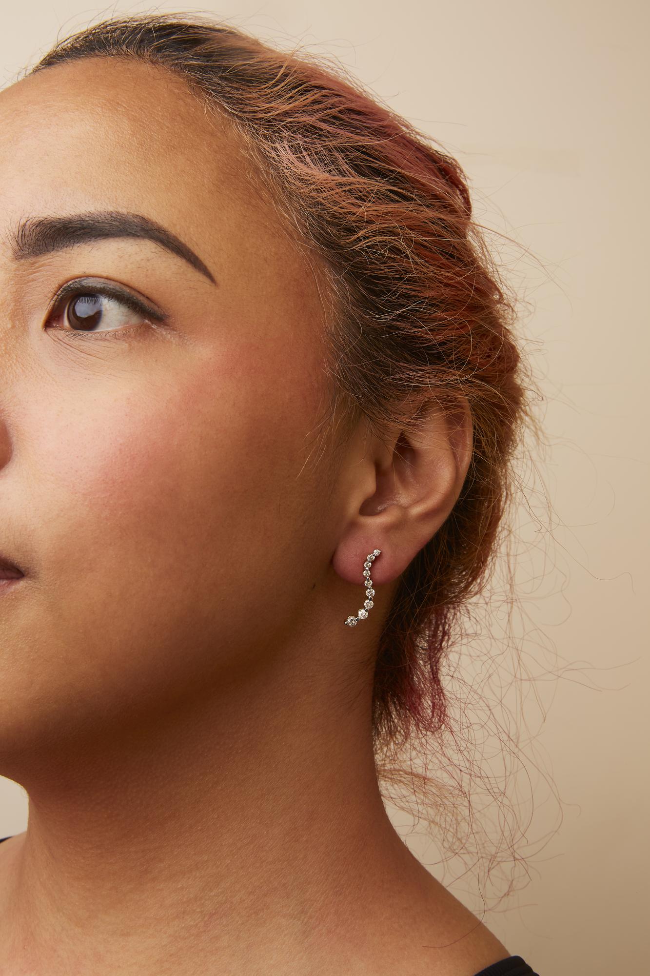 Close-up side view of a yellow metal earring with a curved design featuring multiple round white gemstones in prong settings, worn on a model.