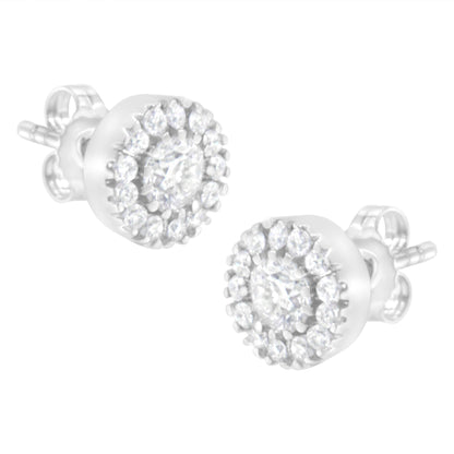 Close-up side angle of a pair of white metal stud earrings featuring a central round prong-set white gemstone surrounded by a halo of smaller round pave-set white gemstones.