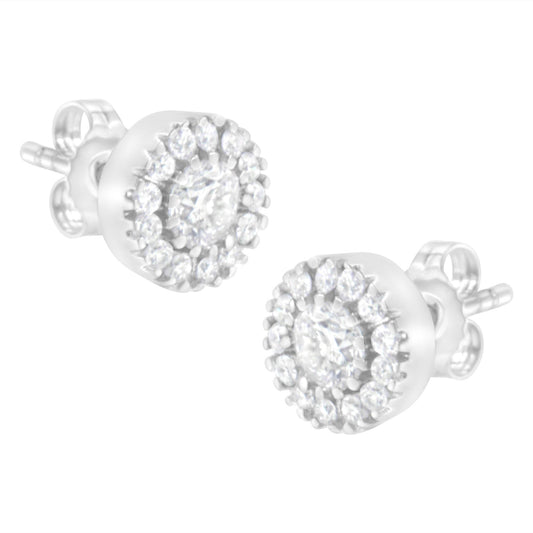 Close-up side angle of a pair of white metal stud earrings featuring a central round prong-set white gemstone surrounded by a halo of smaller round pave-set white gemstones.
