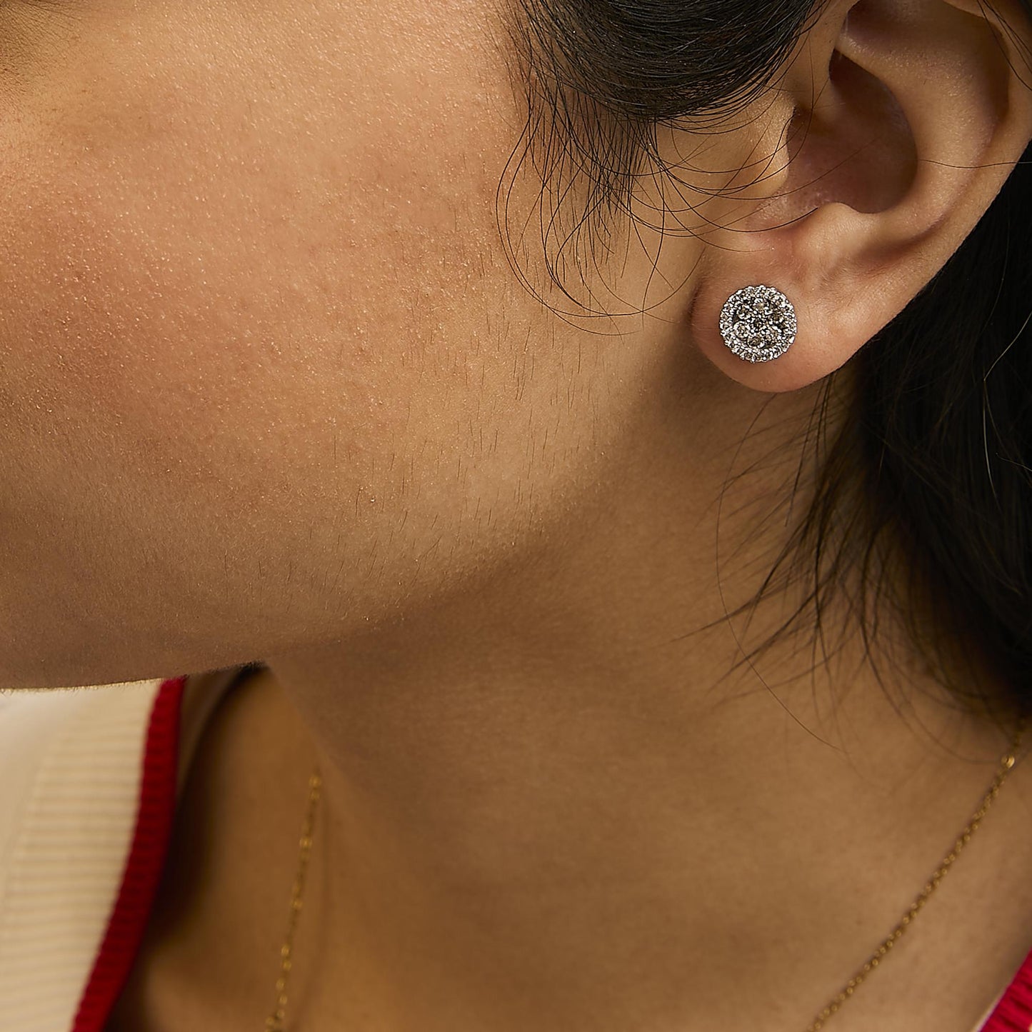 Close-up side-angle of a model wearing white metal stud earrings set with multiple small white gemstones.