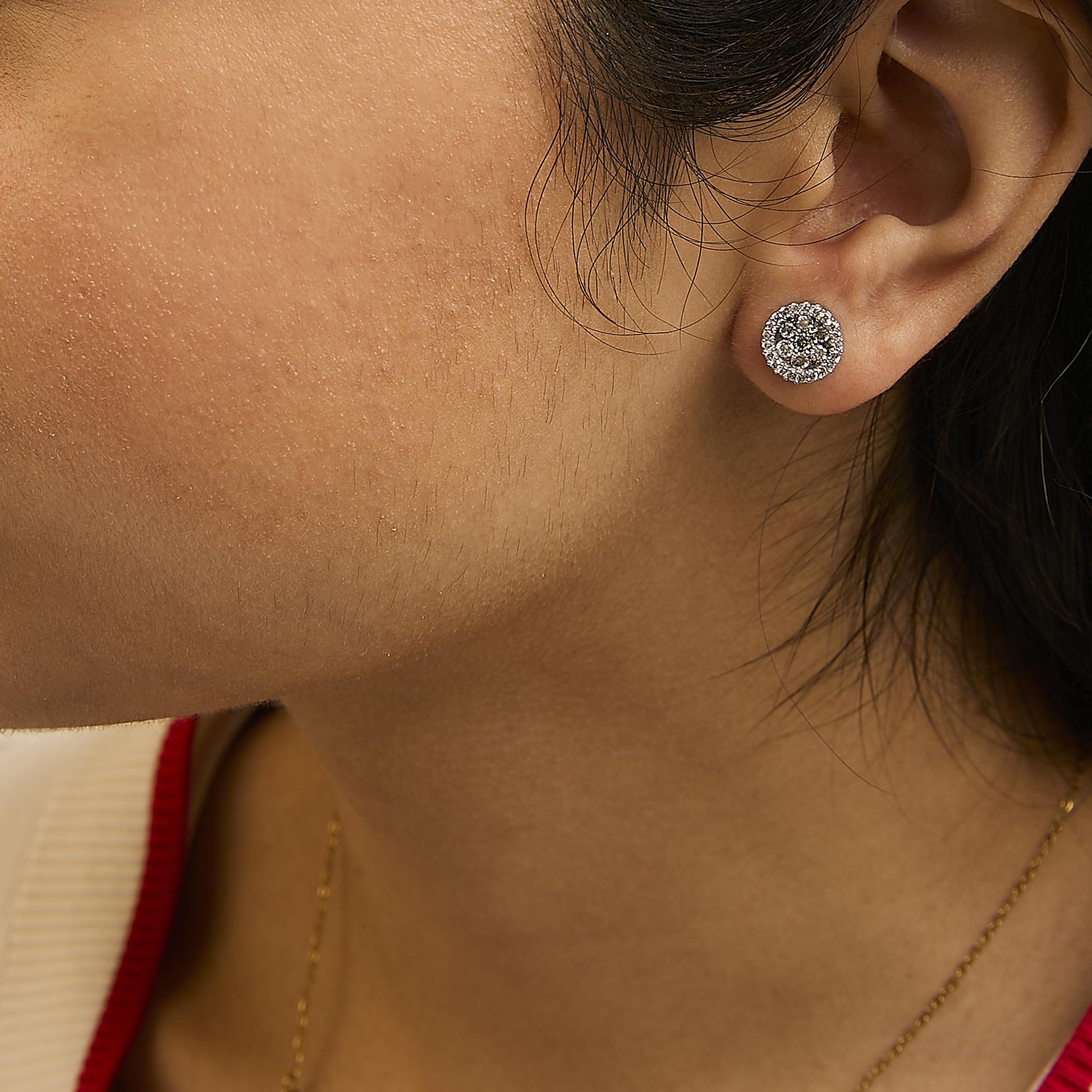 Close-up side-angle of a model wearing white metal stud earrings set with multiple small white gemstones.