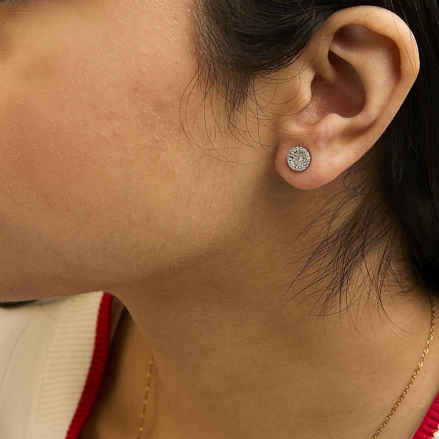 Close-up side view of a white metal stud earring with round white gemstones in a prong setting worn on a model's ear.