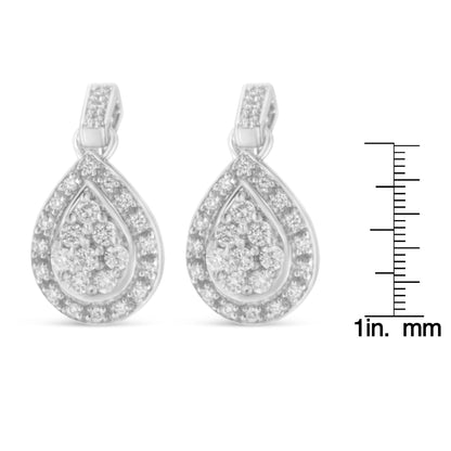 Front view of white metal teardrop-shaped earrings with prong-set round white gemstones, shown next to a ruler for size reference.