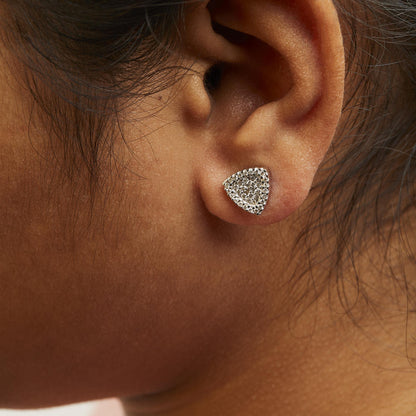 Close-up side view of an ear wearing a white metal triangular-shaped earring with multiple round white gemstones in prong settings.