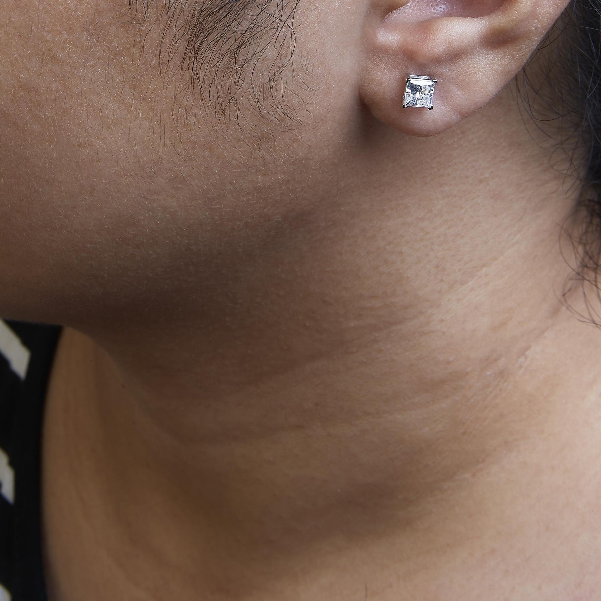 Close-up side view of a white metal princess shape stud earring with a white gemstone in a four-prong setting, worn on a model.