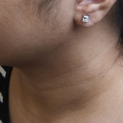Close-up side view of a white metal princess shape stud earring with a white gemstone in a four-prong setting, worn on a model.