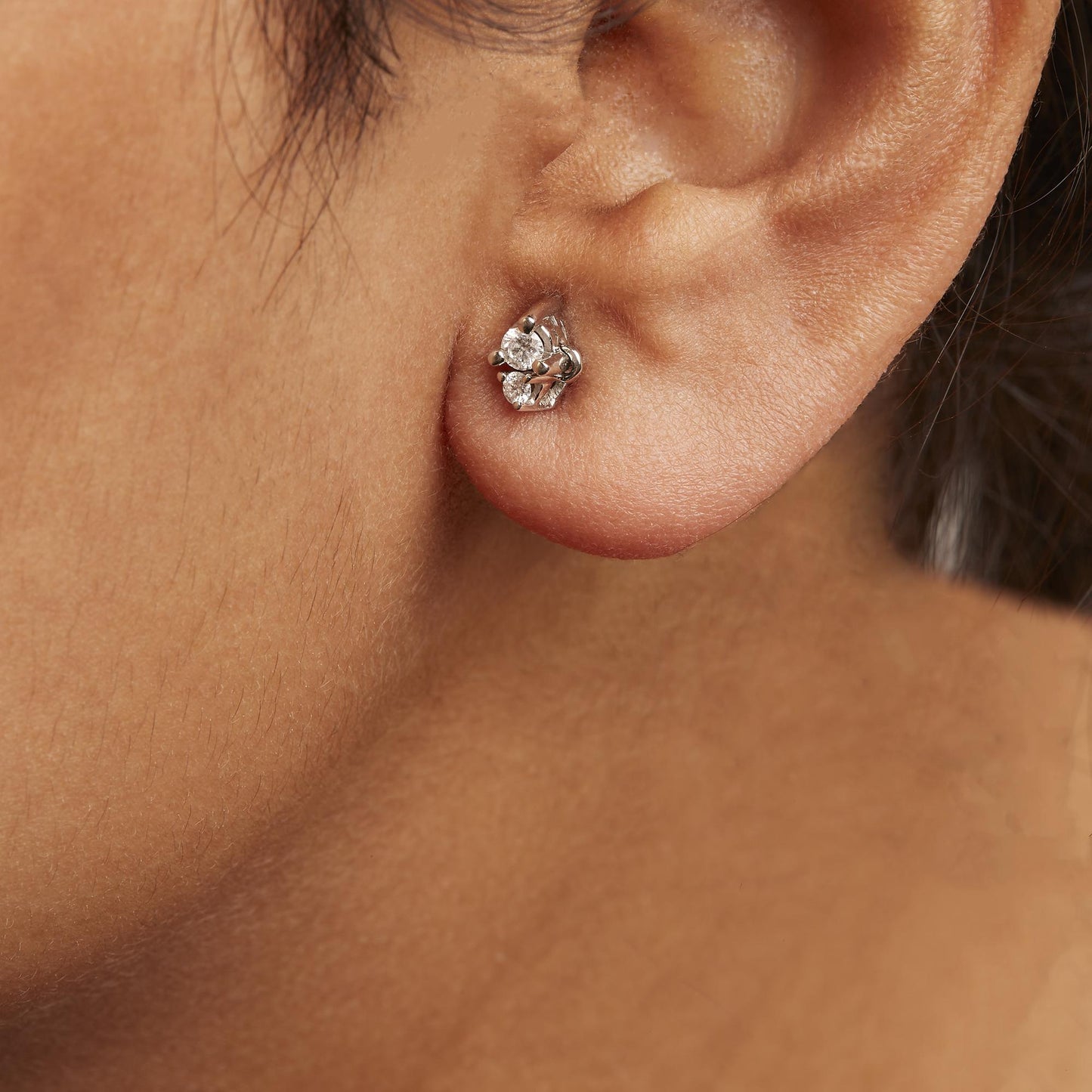 Close-up side view of a white metal earring with two round white gemstones in 3-prong settings, worn on a model.