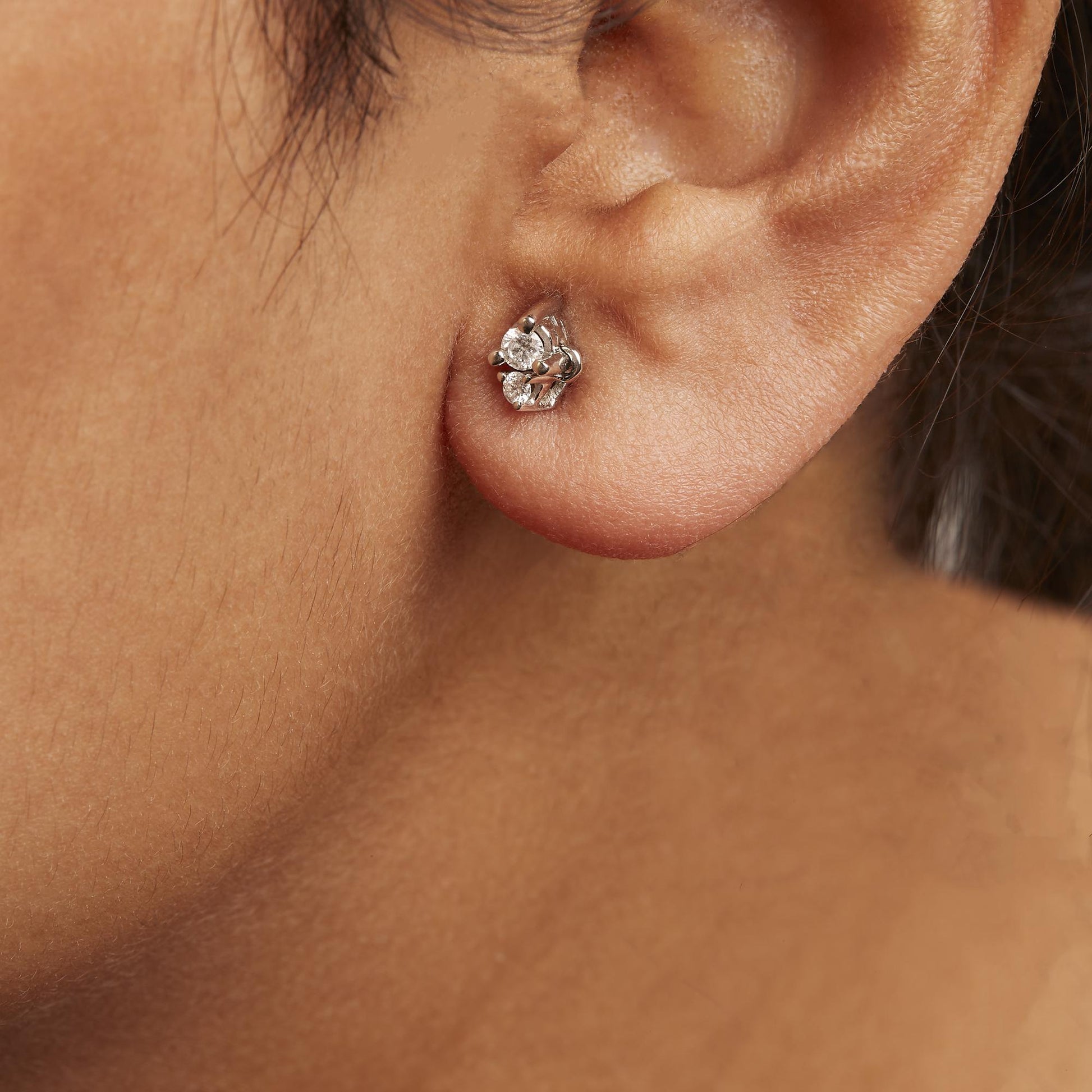Close-up side view of a white metal earring with two round white gemstones in 3-prong settings, worn on a model.
