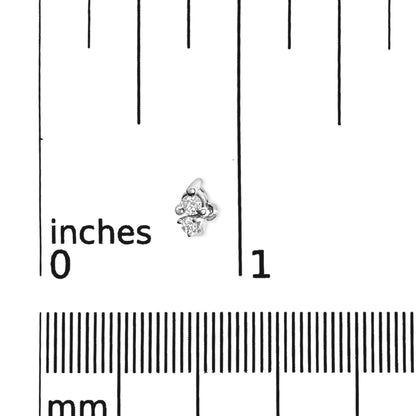 Close-up angled view of a white metal earring with two small round white gemstones in three-prong settings, placed on a ruler for size reference.