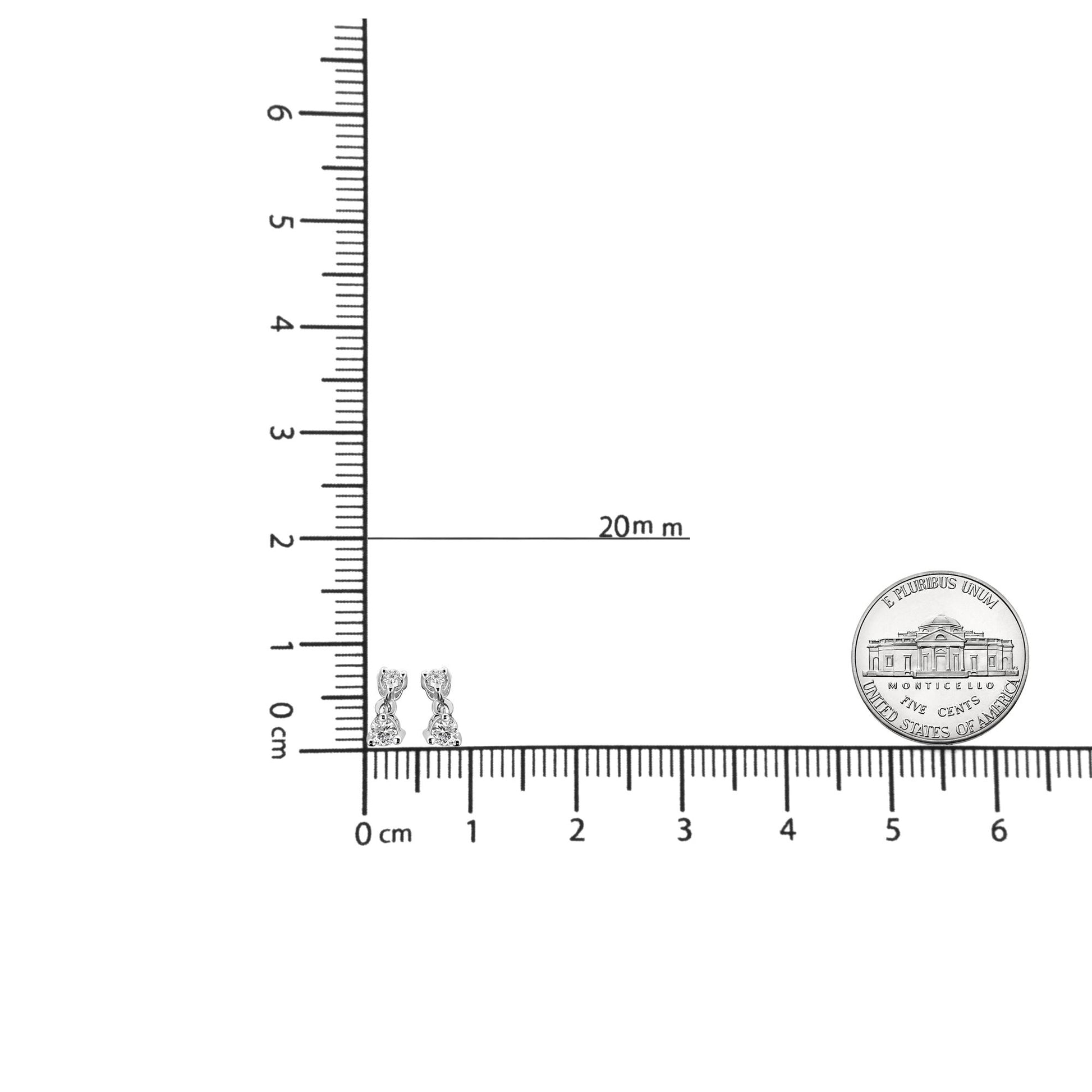 Close-up angled front view of white metal drop earrings with two round white gemstones in prong settings, shown on a ruler for size reference.