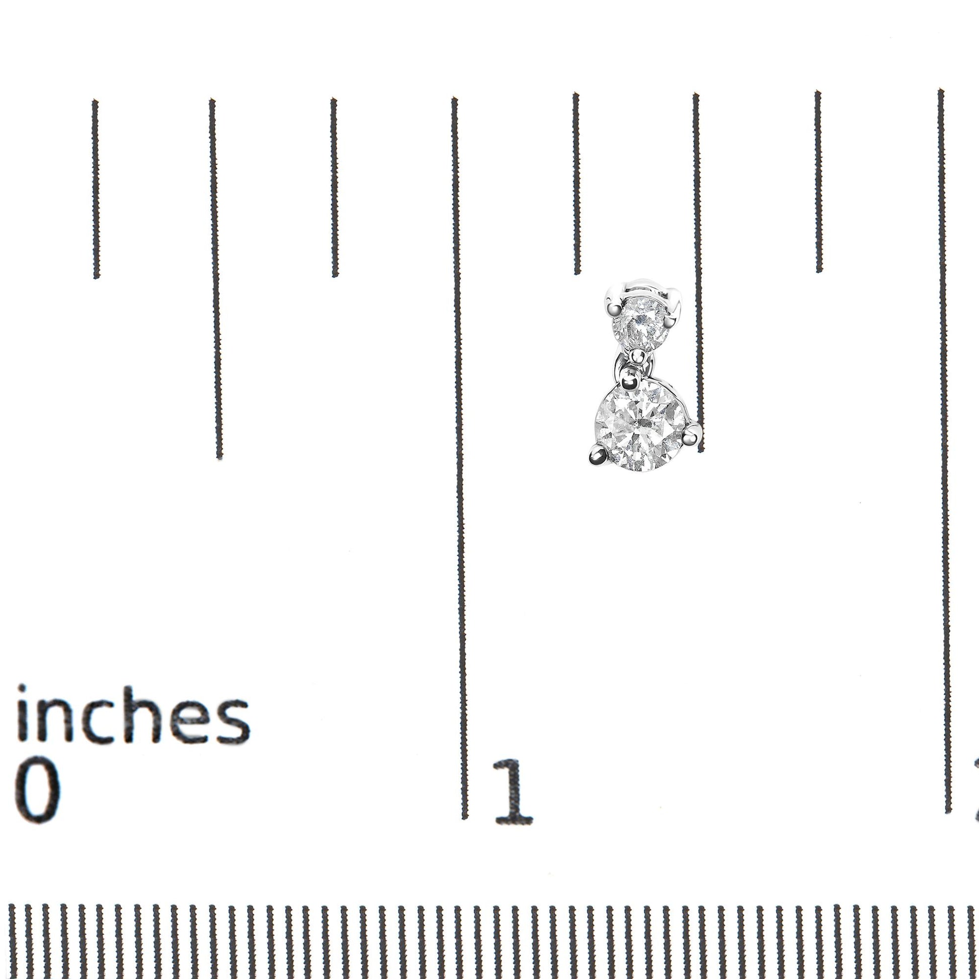 Close-up front view of white metal earrings with two round white gemstones in prong settings, shown on a ruler for size reference.