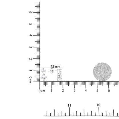 White metal earrings with princess shape white gemstones in prong settings, shown flat on a ruler and scale with a coin for size reference, top-down angle.