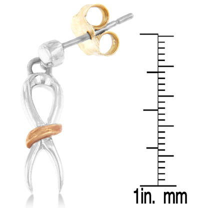 Close-up side view of two-toned metal earrings shaped like an abstract figure eight with a curved band crossing the lower part, shown next to a ruler for size reference.