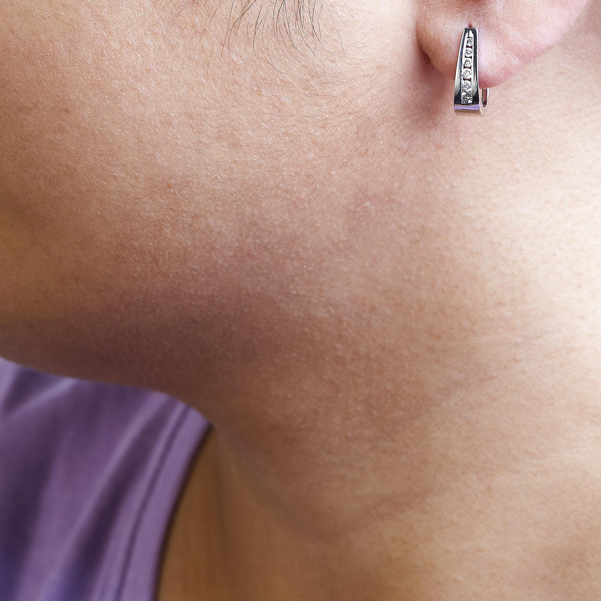 Close-up side view of a white metal earring with a channel setting of round white gemstones worn on a model's ear.